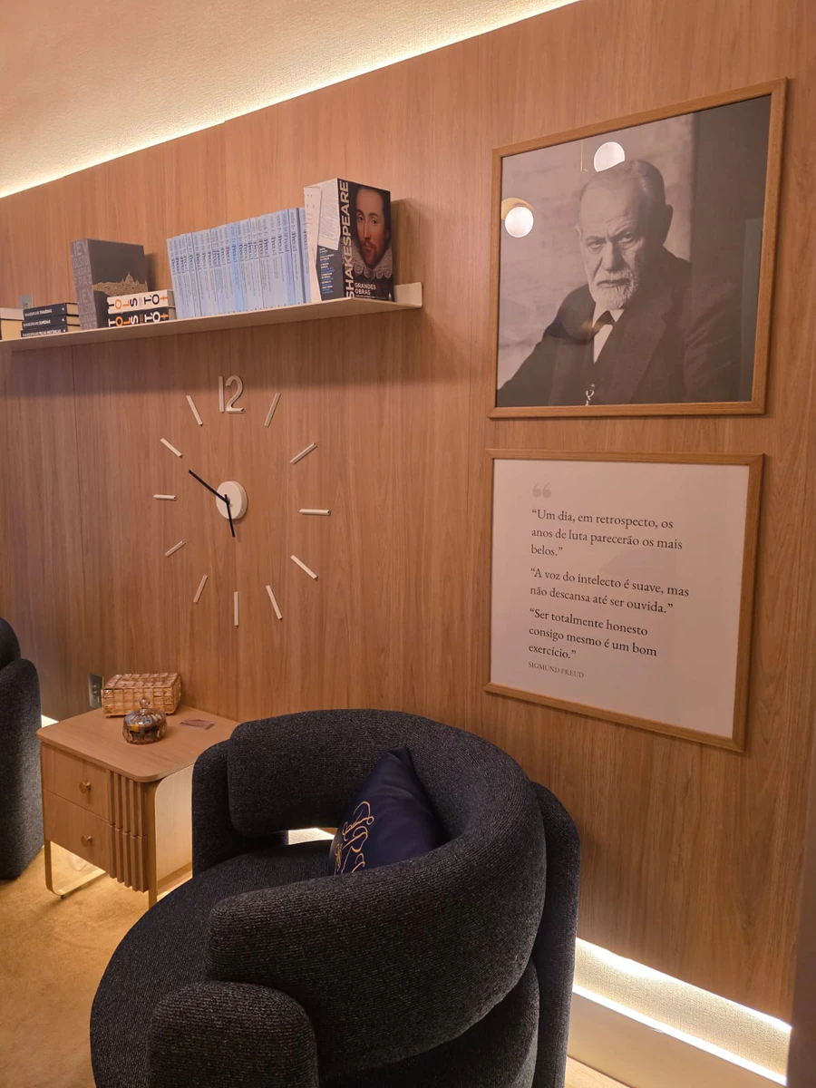 Sala de atendimento com parede de madeira, relógio minimalista, prateleira de livros e retrato de Freud